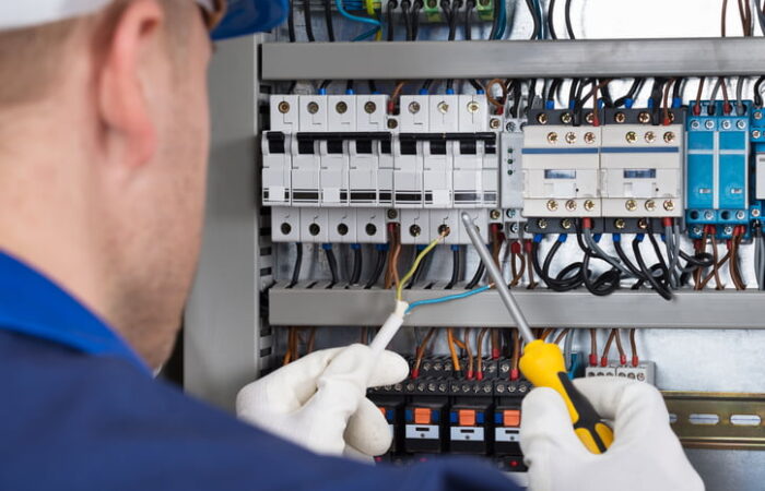 Male Electrician Working On Fusebox With Screwdriver